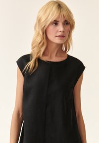 Schwarzes Leinen-Top ohne Ärmel mit rundem Halsausschnitt und subtilen Faltendetails, das über eine glatte Textur und eine lockere Passform verfügt.