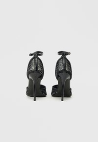 Zapatos de tacón negro con parte superior de malla, tira en el tobillo, detalles de tachuelas en el tacón y un acabado brillante y elegante.
