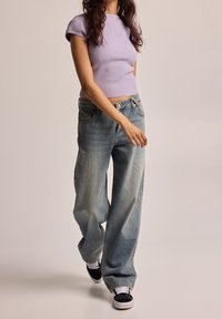 Světle fialový žebrovaný top s krátkým rukávem, zkombinovaný s volnými, vybledlými modrými džíny. Celek doplňují černobílé tenisky.