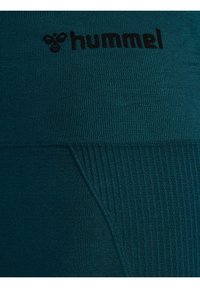 Teal Hummel leggings med en slät, elastisk textur och ribbade detaljer samt en svart logotryck nära midjan.