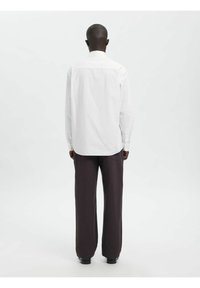 Weißes Langarmhemd mit vertikalen Streifen, Rückansicht; kombiniert mit braunen Hosen mit weitem Bein und schwarzen Schuhen. Glatte Stoffstruktur.