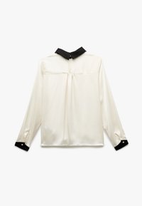 Blusa de manga larga en seda color crema con cuello negro. Presenta puños abotonados y un pliegue en la parte posterior para un detalle adicional.
