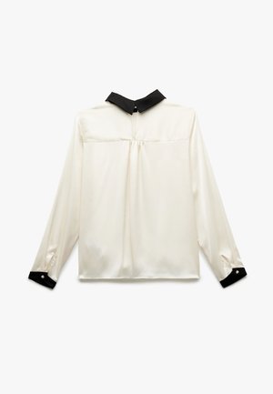 Langsleeve blouse van crèmekleurige zijde met een zwarte kraag. Voorzien van knoopmanchetten en een plooitje op de rug voor extra detail.