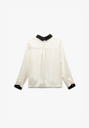 Bluse mit langen Ärmeln aus cremefarbener Seide und einem schwarzen Kragen. Verfügt über geknöpfte Manschetten und eine Falte auf der Rückseite für zusätzliche Details.