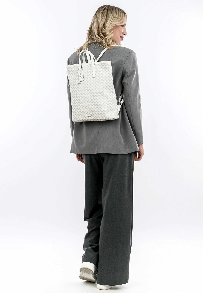 Zaino in pelle bianca con texture geometrica e maniglie superiori, indossato da una persona in un completo grigio, dotato di spallacci regolabili e hardware minimale.