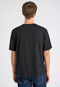 Camiseta de algodón negra con un corte relajado, mangas cortas y cuello redondo. Diseño simple sin patrones ni acentos visibles.