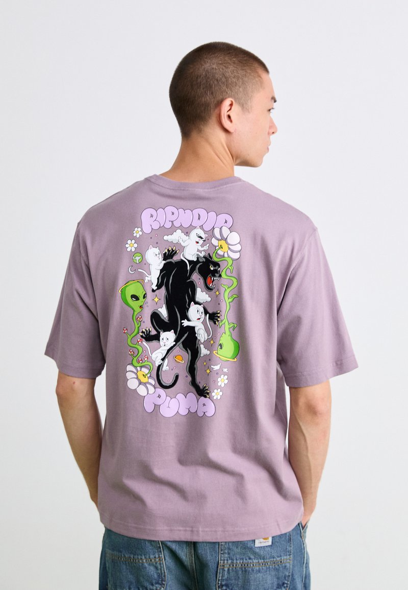Mand iført en lilla t-shirt med et farverigt grafik af en sort panter, hvide katte, grønne rumvæsener, blomster og teksten "Ripndip Puma" på ryggen.