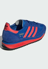 Modré semišové tenisky s červenými akcenty, se třemi pruhy, gumovou podešví a polstrovaným jazykem. Název modelu: adidas SL '72.