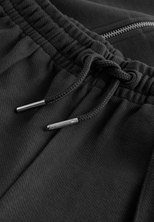 Schwarze Sportshorts aus einem strukturierten Fabric, mit elastischem Bund, Kordelzug mit metallischen Enden und einer kleinen Reißverschlusstasche.