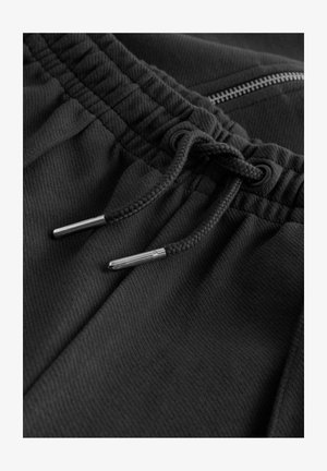 Schwarze Sportshorts aus einem strukturierten Fabric, mit elastischem Bund, Kordelzug mit metallischen Enden und einer kleinen Reißverschlusstasche.