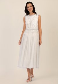 Vestido midi blanco con cuerpo de encaje y mangas con borde festoneado, tela texturizada con lunares y una falda fluida. Tacones plateados con tiras.