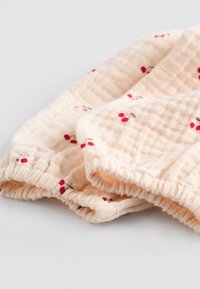Tissu de couleur pêche clair avec un tissage gaufré texturé, agrémenté de motifs épars de cerises rouges. Bords élastiqués pour un ajustement parfait.
