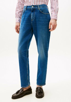 Blauwe spijkerbroek met een rechte pasvorm, featuring een hoge taille, vijf zakken en subtiele vervaging. Gecombineerd met bruine instappers.