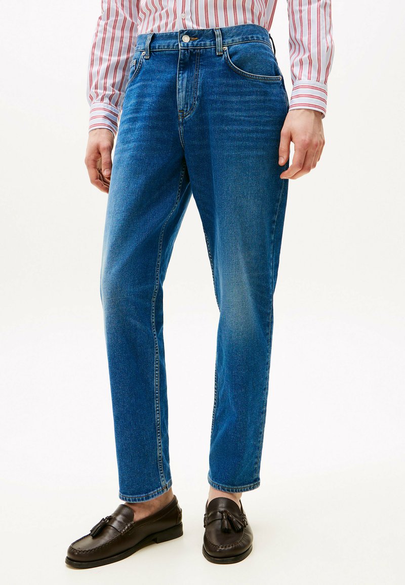 Jeans de mezclilla azul con corte recto, que presentan una cintura alta, diseño de cinco bolsillos y un ligero desgaste. Combinados con mocasines marrones.