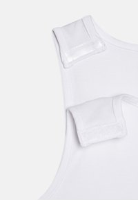 Débardeur blanc en tissu doux, avec encolure arrondie et bretelles auto-agrippantes pour un ajustement réglable. Sans motifs ni accents supplémentaires.
