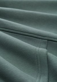 Tela suave y texturizada en un color verde apagado, con costuras suaves y uniformes y un diseño plegado que resalta su flexibilidad.