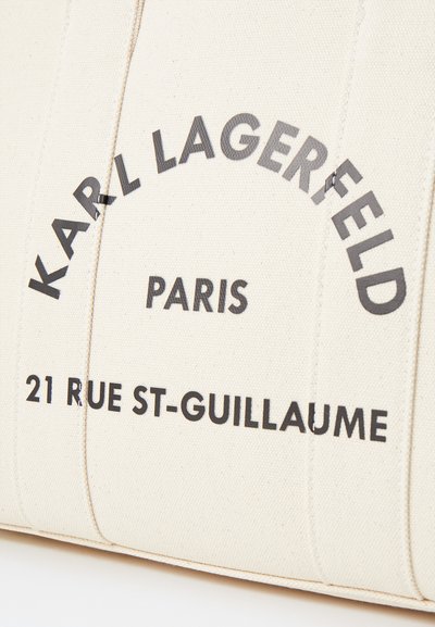 Канадска чанта в кремав цвят с черен текст, който гласи "KARL LAGERFELD PARIS 21 RUE ST-GUILLAUME", с шити детайли и правоъгълна форма.