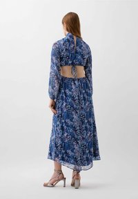 Abito lungo fluido di colore blu con stampa floreale astratta. Presenta maniche lunghe, schiena scoperta e una cintura regolabile in vita.