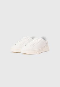 Sneakers casual bianchi a punta bassa con lacci, colli imbottiti e suole spesse testurizzate su uno sfondo chiaro e semplice.