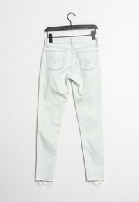 Jeans skinny bleu clair en denim, avec un ourlet effiloché, deux poches arrière avec des coutures incurvées et un patch de marque au-dessus de la poche droite.