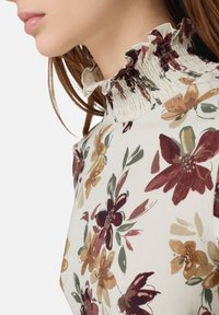 Weiße Bluse mit floralen Mustern und hohem, gerafftem Ausschnitt. Der Stoff zeigt mehrfarbige Blumen in Burgunder, Senf und Grün.