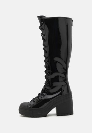 Botas de charol negras hasta la rodilla con un grueso tacón cuadrado, que cuentan con un diseño de cordones frontal y una suela texturizada para mayor tracción.