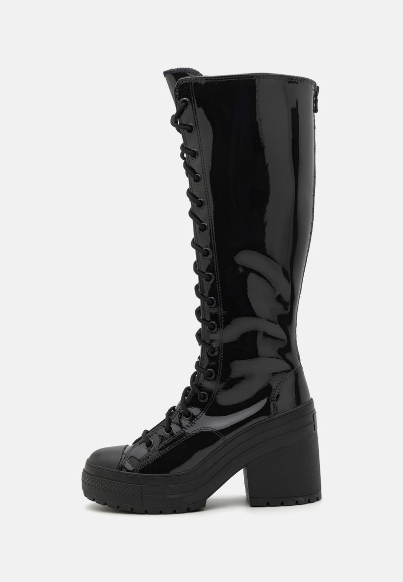 Zwarte lakleren kniehoge laarzen met een dikke blokhak, met een vetersluiting aan de voorkant en een gestructureerde zool voor grip.