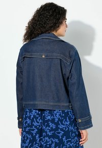 Krátká tmavě modrá džínová bunda se stříbrnými knoflíky, viditelným šitím a klasickým límcem. Nenošena přes vzorované modré šaty.