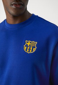 Sudadera azul de algodón, con un logo bordado amarillo del FC Barcelona en el pecho izquierdo. El diseño incluye un cuello redondo.