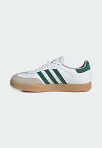 Weißer Sneaker mit grünen Streifen und einer beigen Gummisohle. Verfügt über eine Wildlederspitze und einen gepolsterten Kragen für zusätzlichen Komfort. Schnürdesign.