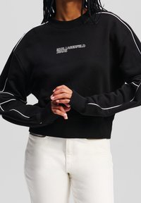 Černá zkrácená mikina s bílými akcenty, žebrovanými manžety a kulatým výstřihem, na přední straně s logem "KARL LAGERFELD JEANS".