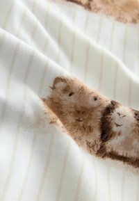 Baumwollstoff in einem hellen Cremefarbton mit einem subtilen Streifenmuster und Illustrationen von zwei braunen, pelzigen Tieren.