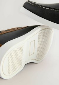 Baskets en cuir noir avec accents marron, semelle en caoutchouc blanc et détails cousus. Semelle extérieure texturée pour une meilleure adhérence. Design décontracté.
