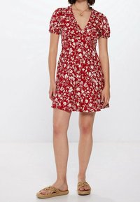 Rotes Blumendruckkleid mit kurzen Puffärmeln und V-Ausschnitt. Ausgestellter Saum, leichtes Material, passt gut zu beigen, geflochtenen Sandalen.