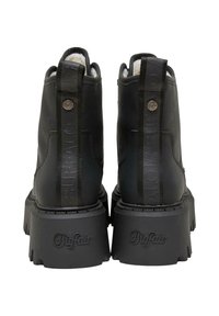 Paire de bottines en cuir noir avec des semelles épaisses crantées, marquées "Buffalo" sur le talon et les languettes arrière, vues de dos.