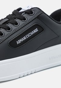 Mustast nahast sneakers valge kummitaldaga. Omab tikandiga disaini, musti paelu ja valget 'ARMANI EXCHANGE' logo küljes.