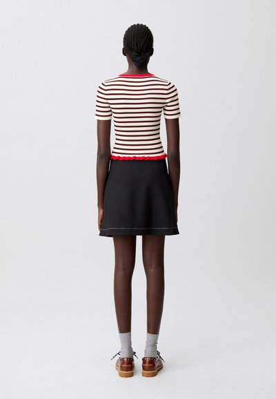 Top ajustado a rayas en crema y burdeos con bajo rojo con volantes, combinado con una falda negra skater, calcetines grises y zapatos marrones.