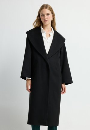 Lange zwarte jas met een brede kraag, gestructureerd ontwerp en klokvormige mouwen. Bevat zijzakken en een strakke stikselafwerking.