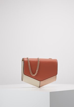 Sac à main en cuir bicolore marron et beige avec bord inférieur triangulaire et bandoulière chaîne dorée reposant sur une surface blanche sur un fond uni.