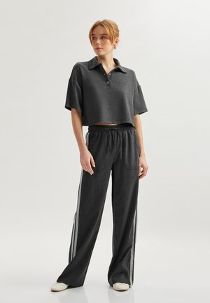 Mørkegrå beskåret polo-shirt med krave og knapdetaljer, parret med løstsiddende mørkegrå bukser med sidelister og lommer.