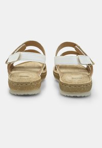Valkoiset remmisandaalit, joissa on teksturoitu beige pohja, säädettävä solki ja kumipohja, jossa on pito-kuvio.