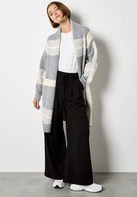 Cardigan largo a rayas grises y crema hecho de lana suave, combinado con pantalones de pierna ancha negros y zapatillas blancas. Ajuste simple y relajado.