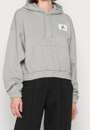 Felpa grigia corta con tasca frontale, cappuccio con coulisse, polsini elasticizzati e una patch con logo sul petto. Tessuto morbido con una finitura texture.