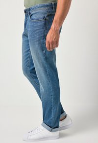 Jeans de denim azul claro con corte recto, un ligero desvanecimiento y un dobladillo enrollado, combinados con zapatillas blancas.