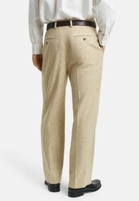 Pantalons en laine beige avec une finition texturée, dotés de deux poches arrière et d'un design à jambe droite, associés à des mocassins noirs.
