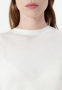 Valge puuvillane T-särk ümmarguse kaelusega. Kanga pind tundub pehme ja veidi läbipaistv, ilma nähtavate mustrite või aktsentideta.