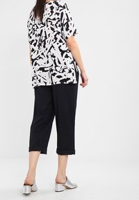 Pantaloni neri a vestibilità ampia abbinati a una maglietta bianca con un motivo geometrico nero. Il modello indossa sandali argento con tacco a blocco.