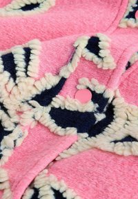 Teksturirana tkanina rožnate barve z vzorci v mornarsko modri in kremni barvi; vključuje okrogel rožnati gumb; mehki, volnenemu podobni videz.