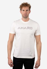 Camiseta blanca de algodón con un logo geométrico "AMARO" en un diseño contrastante. Mangas cortas y cuello redondo con una textura suave.