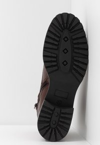 Botte en cuir marron dotée d'une semelle en caoutchouc noir texturée avec un motif en diamants. Fermeture éclair latérale pour un accès facile. Étiquette de taille visible.